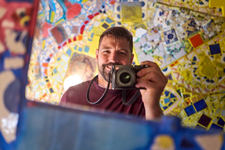 Justin Hawkes, a mirror self-portrait holding a Leica camera against a mosaic-tiled wall